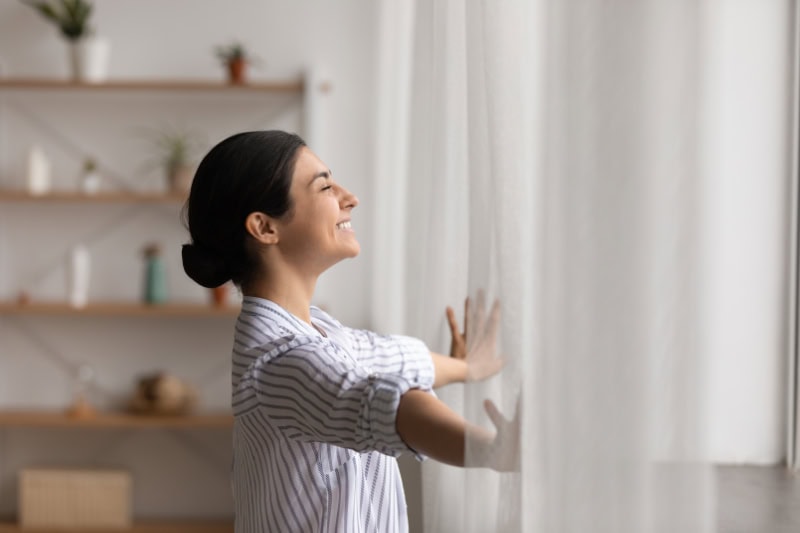 Why Ductless Is the Way to Go. Bathing in sunlight. Excited young indian lady meet first morning at new flat house part curtains enjoy being homeowner. Happy hindu female open drapes on window breath fresh air close eyes in delight.